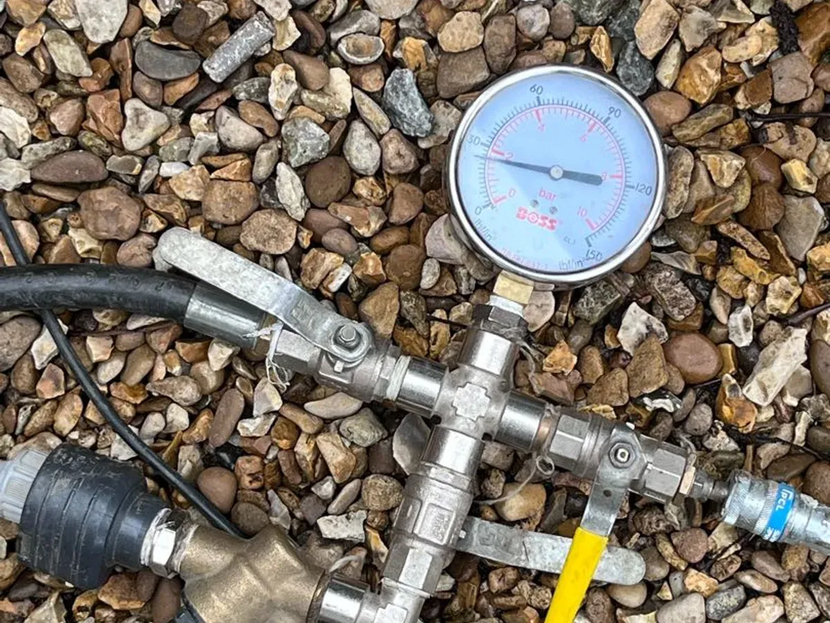 Pressure test manifold with a large gauge, laid on gravel during a heating investigation
